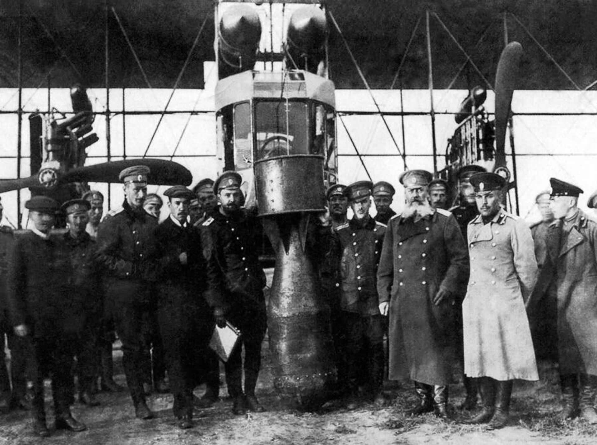 Игорь Сикорский (третий слева, в кепке), Михаил Шидловский (третий справа, в бороде) и 25-пудовая/400 кг. учебная бомба (в центре) Игорь Сикорский (третий слева, в кепке), Михаил Шидловский (третий справа, в бороде) и 25-пудовая/400 кг. учебная бомба (в центре) - РИА Новости, 1920, 18.06.2026