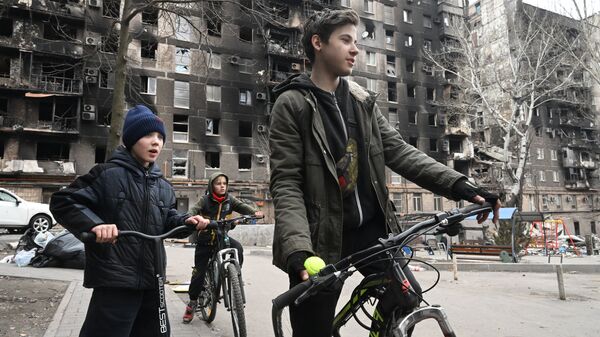 Дети катаются на велосипедах у разрушенных домов в Мариуполе